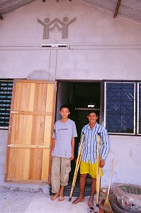 Prayad Santo, on crutches, and his son Sinchai Santo stand in front of their recently completed Habitat house in Udon Thani, Thailand. (2001)