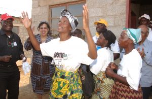 Festivities and dancing at house dedication at house #11 including homeowner Emelda Mbewe, volunteers, UNICEF Zambia leader Dr. Stella Goings (matching blue patterned head piece and outfit) and Kenneth Kaunda (black clothes, red ball cap).  UNICEF provided a large package contribution to this Habitat project which will include several bore holes (for wells), materials for 20 latrines, and meetings with homeowner families to provide each person with a insect repellent coated mosquito net.  (Kenneth Kaunda Work Project 2003)